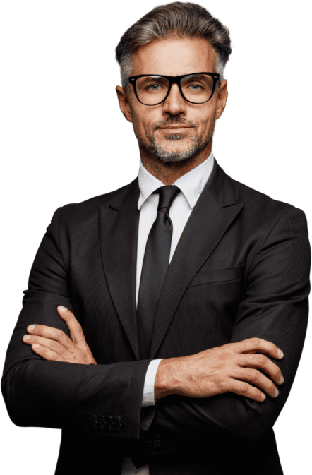 A man with glasses in a black suit and tie stands with arms crossed against a white background.
