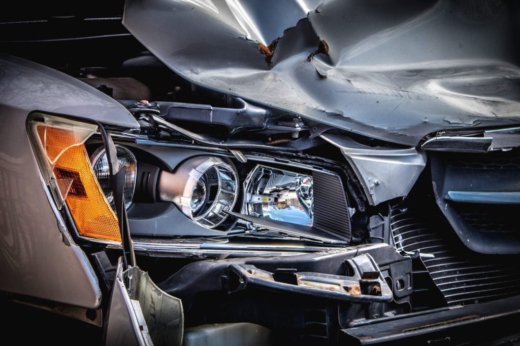 Close-up of a car with significant front-end damage, showing a crumpled hood and exposed headlight after a collision.