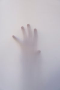 A hand is pressing against a translucent surface, creating a blurred and shadowy outline of the fingers.